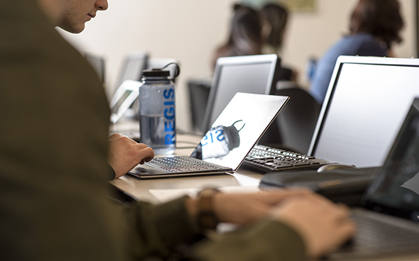 hands typing at computer with Regis water bottle on desk