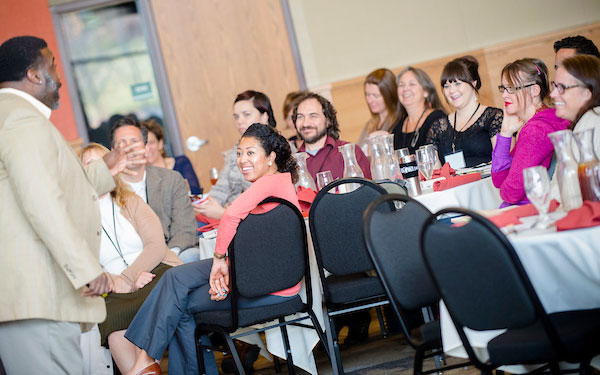 conference attendees smile and observe speaker at the front of the room