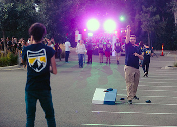 students play cornhole in a parking lot with food trucks in the background