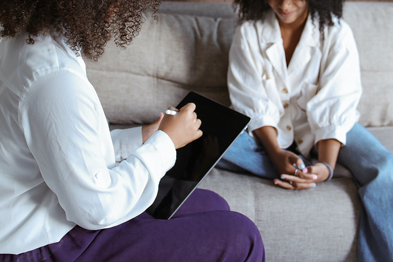 a counselor writes in her notebook while patient sits on a sofa talking