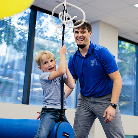 an Regis-Creighton Occupational Therapy student swings a young child on a swing during class