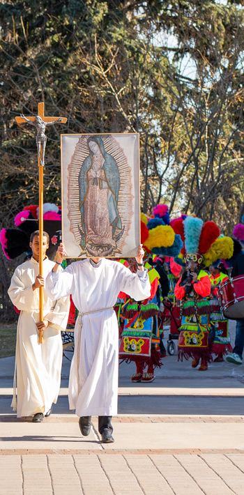 Participants in a Danza de matachines procession carrying a cross and religious image during a cultural and faith event