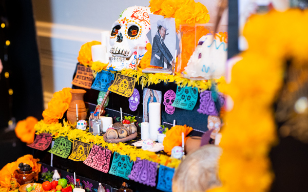 Day of the Dead altar with a colorful sugar skull, marigold flowers, papel picado, candles, and a photo of a man