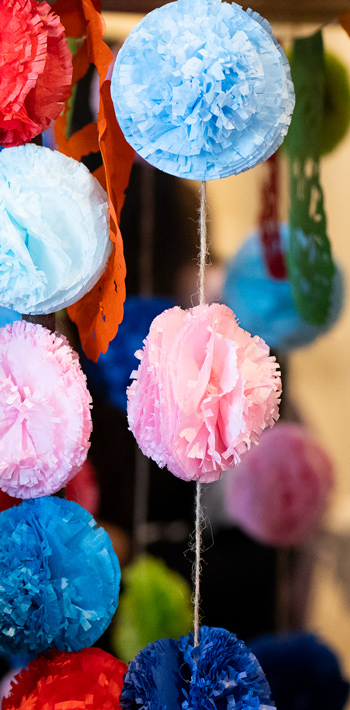 Colorful tissue paper pom-poms and decorations hang on strings, including pink, blue, and red hues, creating a festive atmosphere