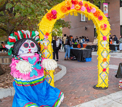 Woman skeleton pinata next to colorful arch lined in colorful paper