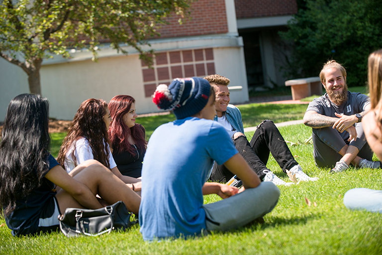 a diverse group of young students sits on the grass on the quad