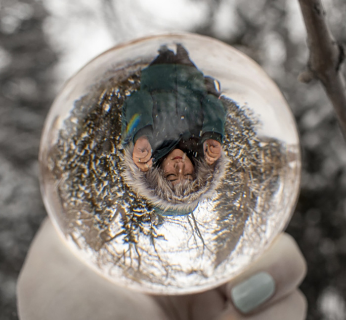 photo of student standing in the snow while wearing a parka reflected in a glass orb