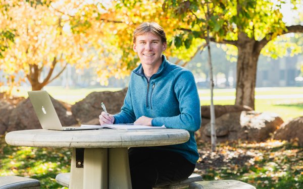 Student with a laptop and a pen and notebook at an outdoor cement table