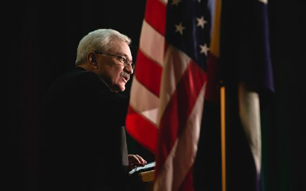 Father Fitzgibbons stands at a podium in front of the American flag