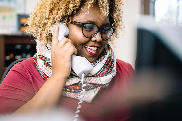 woman speaks on phone, looking at computer