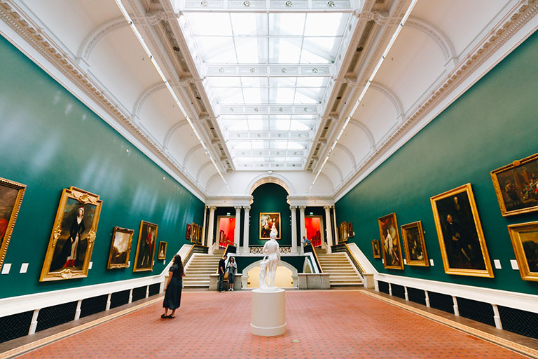 woman and couple enjoying paintings and sculptures in a grand gallery