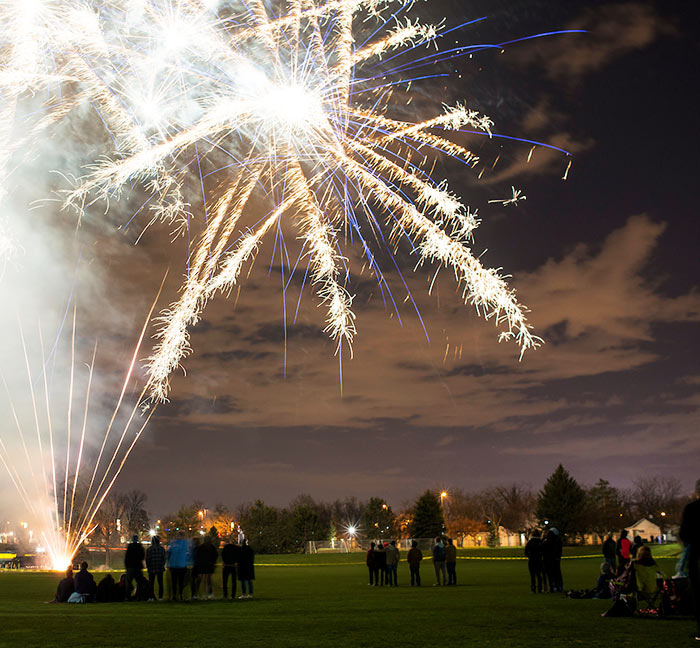 a crowd is silhouetted against a fireworks display on the match pitch on campus