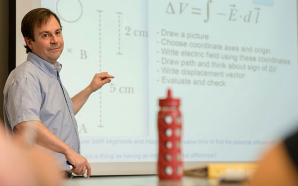 Fred Grey lectures in front of a projector screen displaying mathematic equations