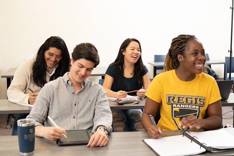 Students in a Regis University Classroom smile while taking notes and engaging in a lively discussion