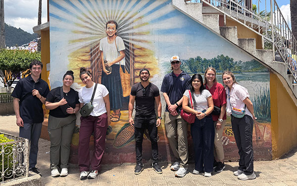 a group of Regis health care students pose in front of a colorful banner during an immersion in South America