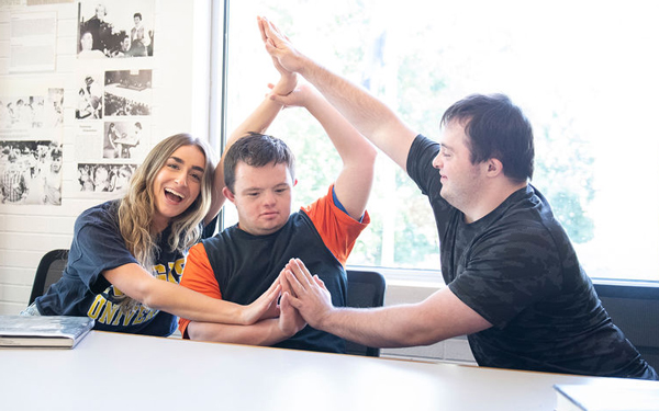 Three students create a playful hand formation at a table in a classroom.
