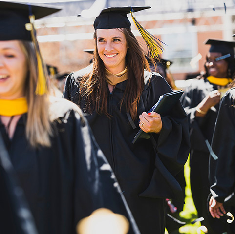 a master's graduate smiles while wearing regalia and recessing from the stage with her peers at the Spring commencement ceremony on the Quad on the Northwest Denver campus