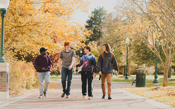 four students walk down sidewalk in fall