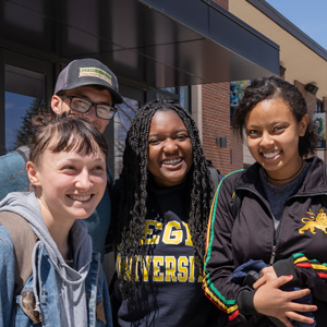 Students stand together outside a campus building at Regis University, smiling on a sunny day with Main Hall in the background