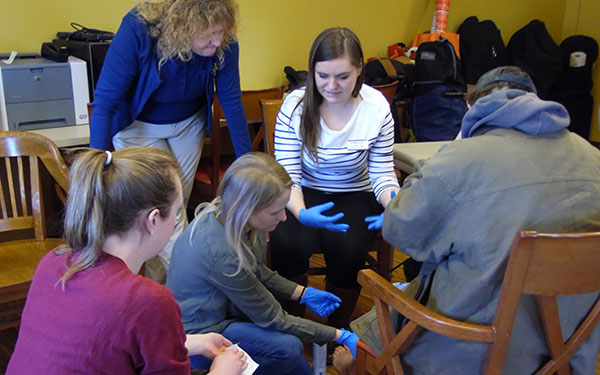 students wearing gloves attend to the feet of a man seated in a chair