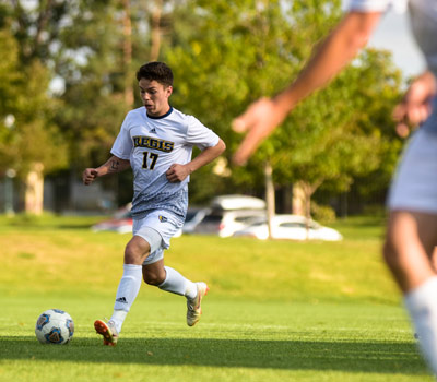 Regis men's soccer player, number 17, setting up to kick the soccer ball to a teammate