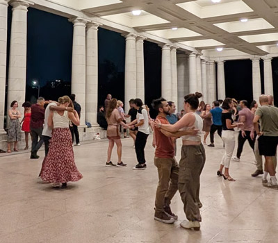 Groups of couples salsa dancing under lit park pavilion