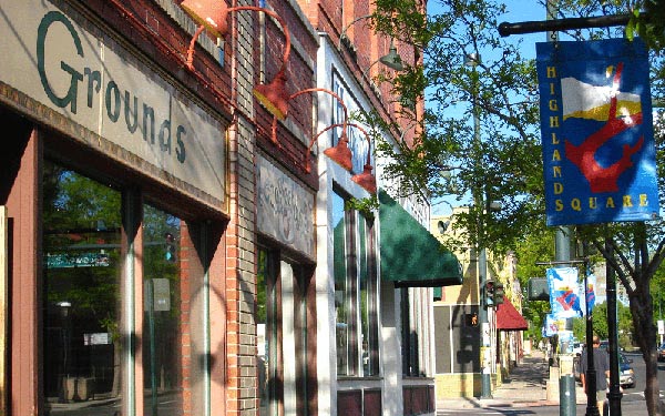 Shops and business line a shady sidewalk in the Highlands Square Neighborhood