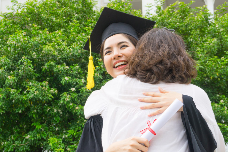 a graduate in regalia hugs a woman