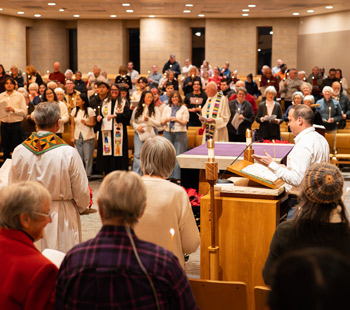Students, faculty, and community members participating in a candlelight service in a campus chapel.