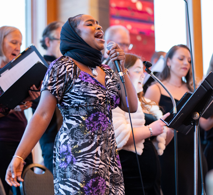 Student singing a solo into a microphone with a choir during a live performance