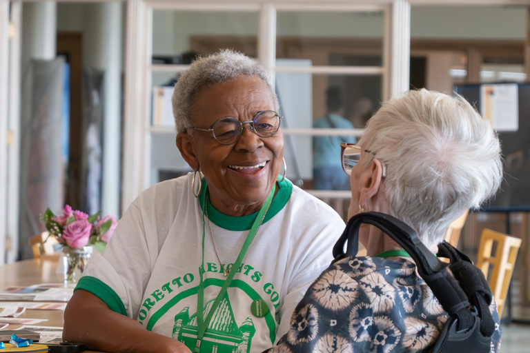 Two elderly women, who are Loretto Heights College alumni, share a warm conversation and smile at each other
