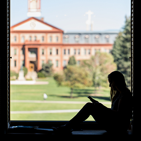 woman studies by window overlooking Main Hall and Boettcher Commons