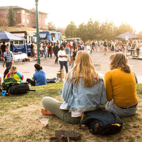 two students sit on grass during student activities event