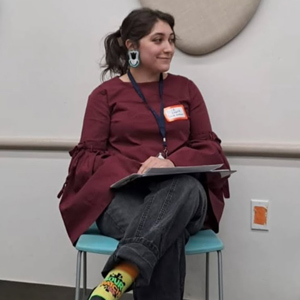 Speaker, Lila Crank, sitting on a chair with legs crossed and looking towards the right