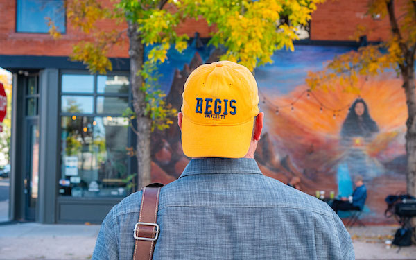man in a Regis University ball cap looking at a mural