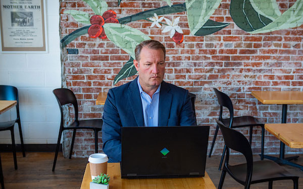 man in professional attire works on a laptop while sitting in a coffee shop