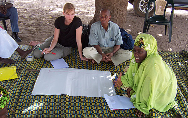 development practice students sit on a colorful cloth while writing