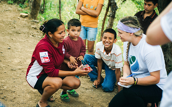 two women squat and smile while children look on