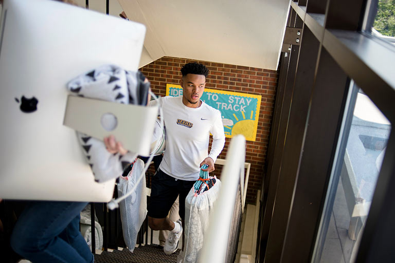 a student and helpers carry a computer, clothes and other belongings up the stairs in the DeSmet Hall dorm