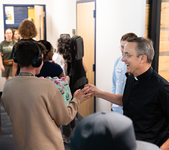 Regis University student greeting a priest in a campus hallway.