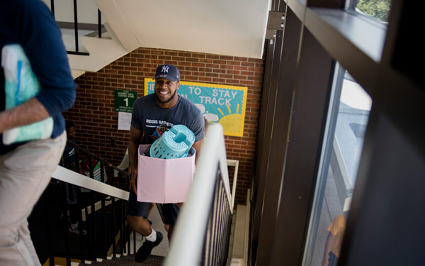 Student smiling and holding a box walking up the stairs in Desmet Hall