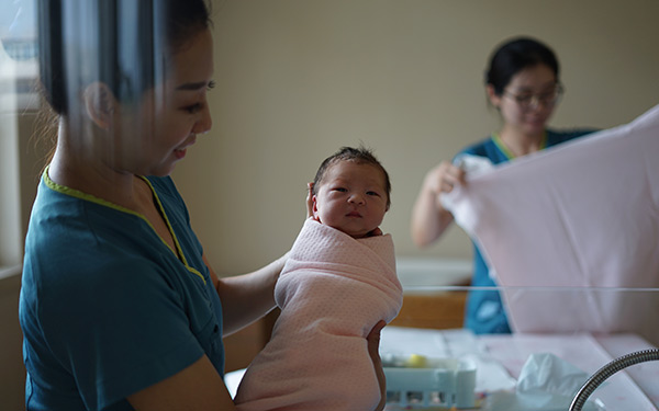 nurse holds newborn up to maternity ward glass