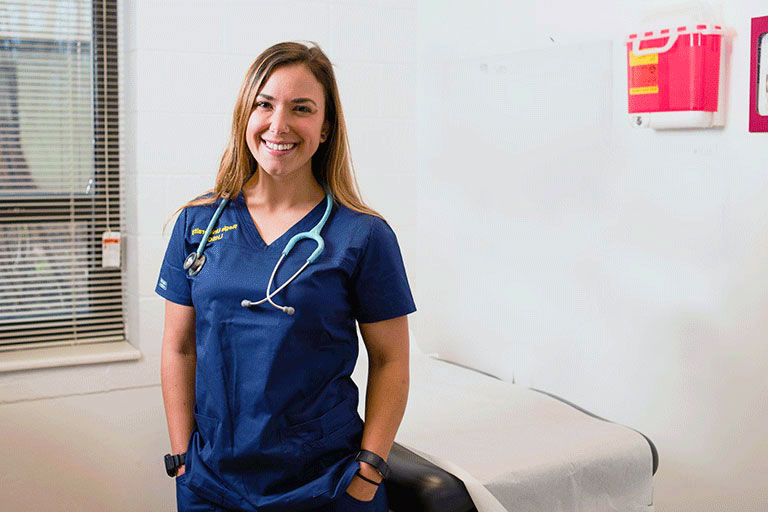a nurse wearing Regis scrubs smiles while standing in an exam room