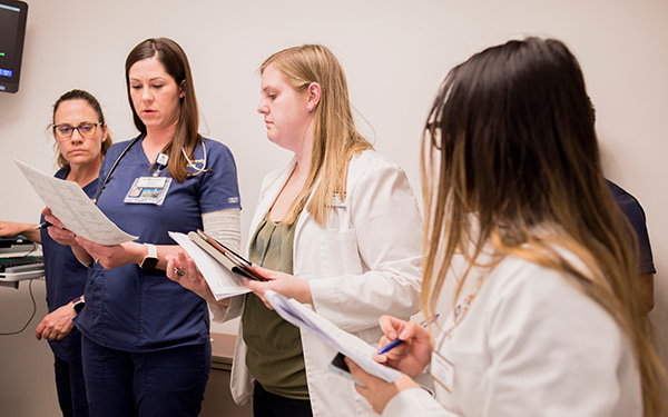 Four nursing students in their scrubs look over paper together. Working hands on in a dummy patient room