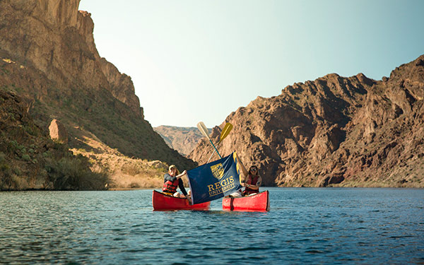 Students kayaking on a lake and holding a Regis University flag