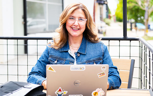 a student in an online graduate program works on a laptop at an outdoor cafe in Denver, Colorado