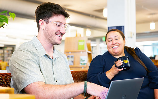 students in online undergraduate programs work together on a laptop in the library on Regis University's campus