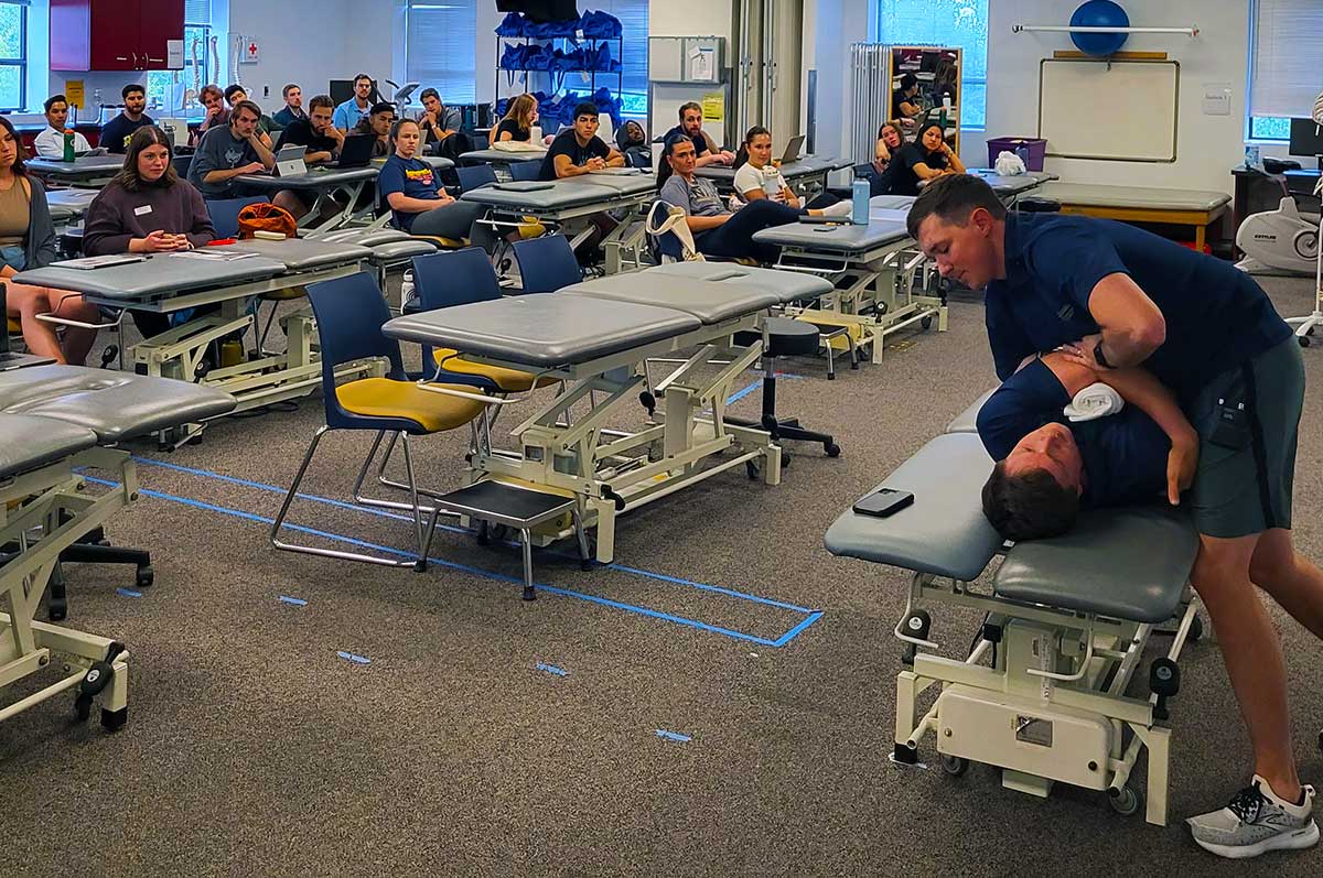 a professor demonstrates a technique on a volunteer while students observe in a Regis PT classroom
