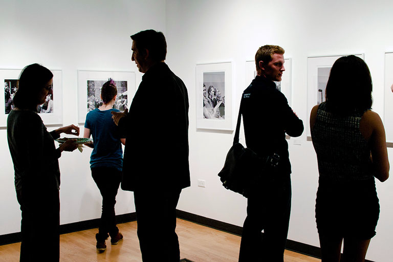 small crowd in an art gallery views artwork on the walls