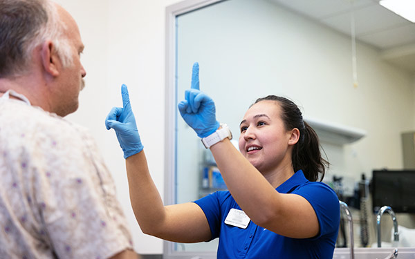 a Regis-Creighton OTD student holds up her hands while checking a patient's visual abilities in a classroom